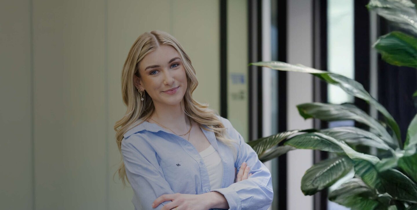 A woman with long blonde hair and earrings folding her arms and smiling towards a camera - ACAP Criminology (1430x952)