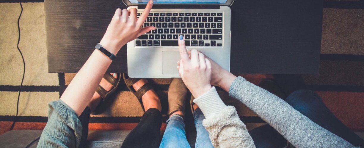 Key dates Aerial view of three students sitting and pointing towards a laptop screen, with only their arms and hands in view