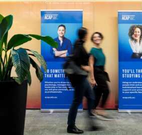 Two people walk in front of banners in hallway.