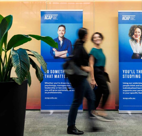 Two people walk in front of banners in hallway.