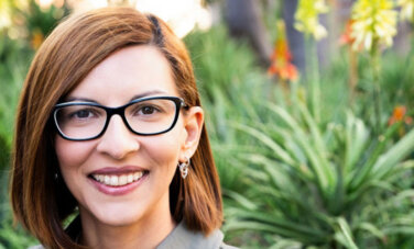 Alice-Viviana Bercean woman with red hair and glasses smiles in front of a background of greenery