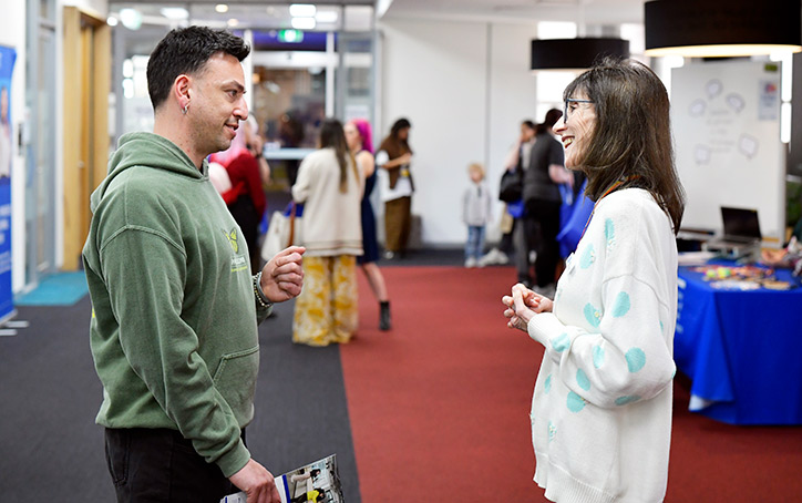 A female ACAP University College staff member standing with and talking to a prospective student at an Info Night event (724x454)