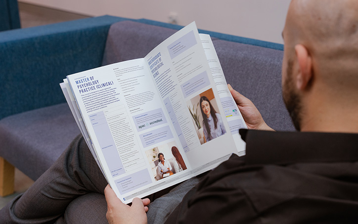 A male prospective student reading a course guide booklet at an ACAP University College Info Night event (724x454)