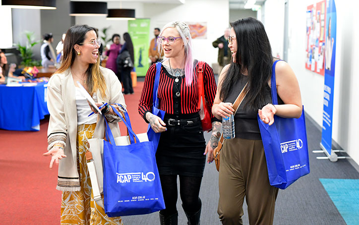 Three prospective students walking and talking with each other, holding ACAP University College tote bags at an Info Night event (724x454)