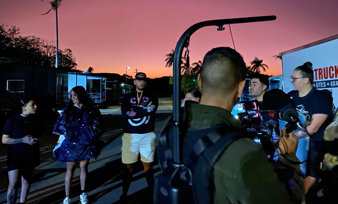 Krunal voice filming image of cameraman shot from behind in a sunset-lit scene flled with young people chatting in a parking lot