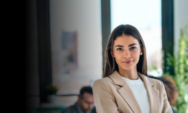 A young woman with long hair and a beige suit jacket in a an office space - wide shot