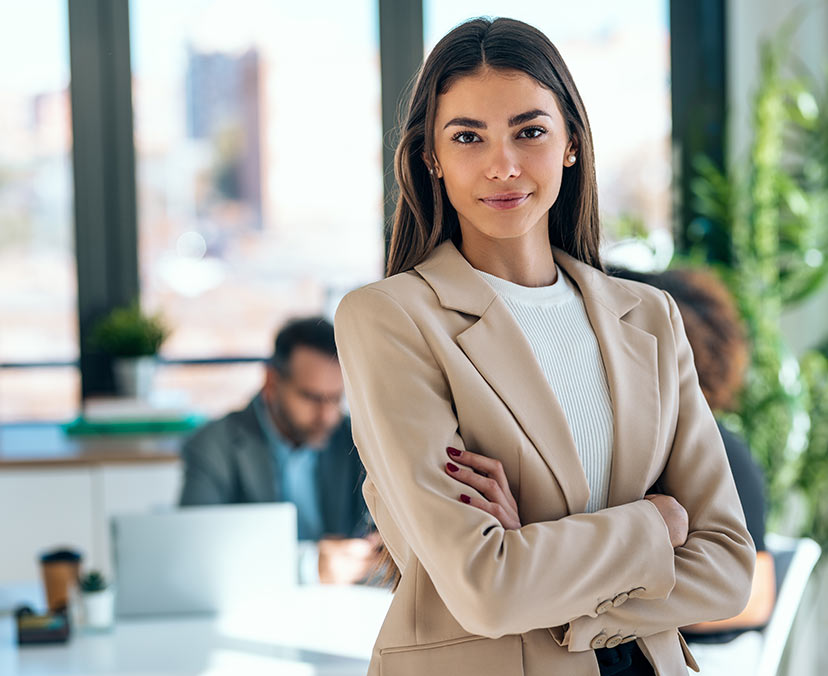 A young woman with long hair and a beige suit jacket in a an office space