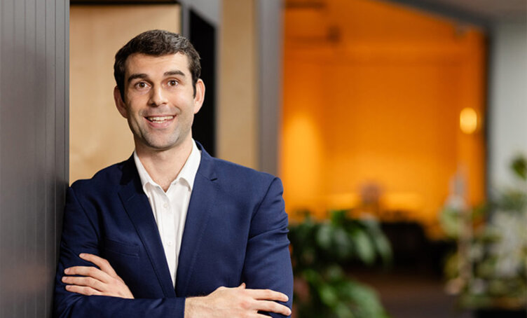 ACAP GDLP alumni Theophilos Thompson standing in an office space wearing a navy blue suit and folding his arms - desktop image