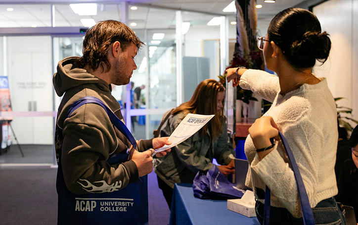 A male student reading a flyer at an ACAP University College Open Day event (724x454)