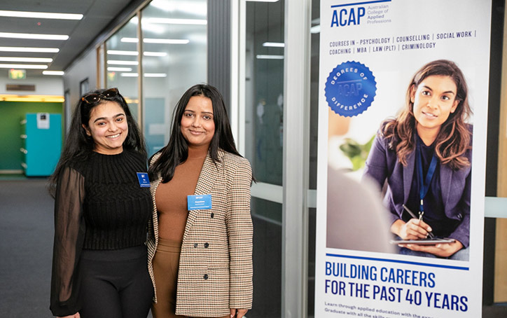 Two course advisors standing next to a sign at an ACAP University College Open Day event (724x454)