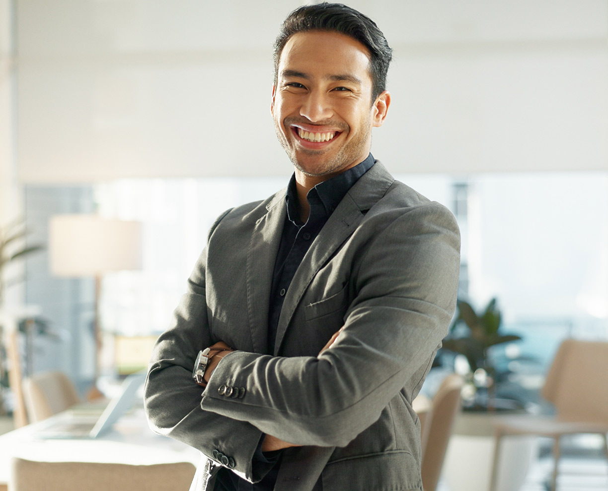A man in a green and black shirt standing in an office with his arms folded, smiling towards camera (1224x990)