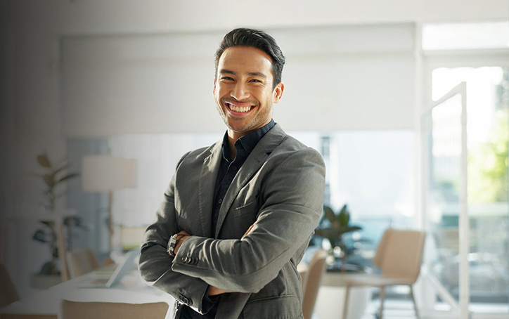 A man wearing a dark green suit, smiling towards camera with his arms folded - Master of Professional Accounting (MPA) - 724x454