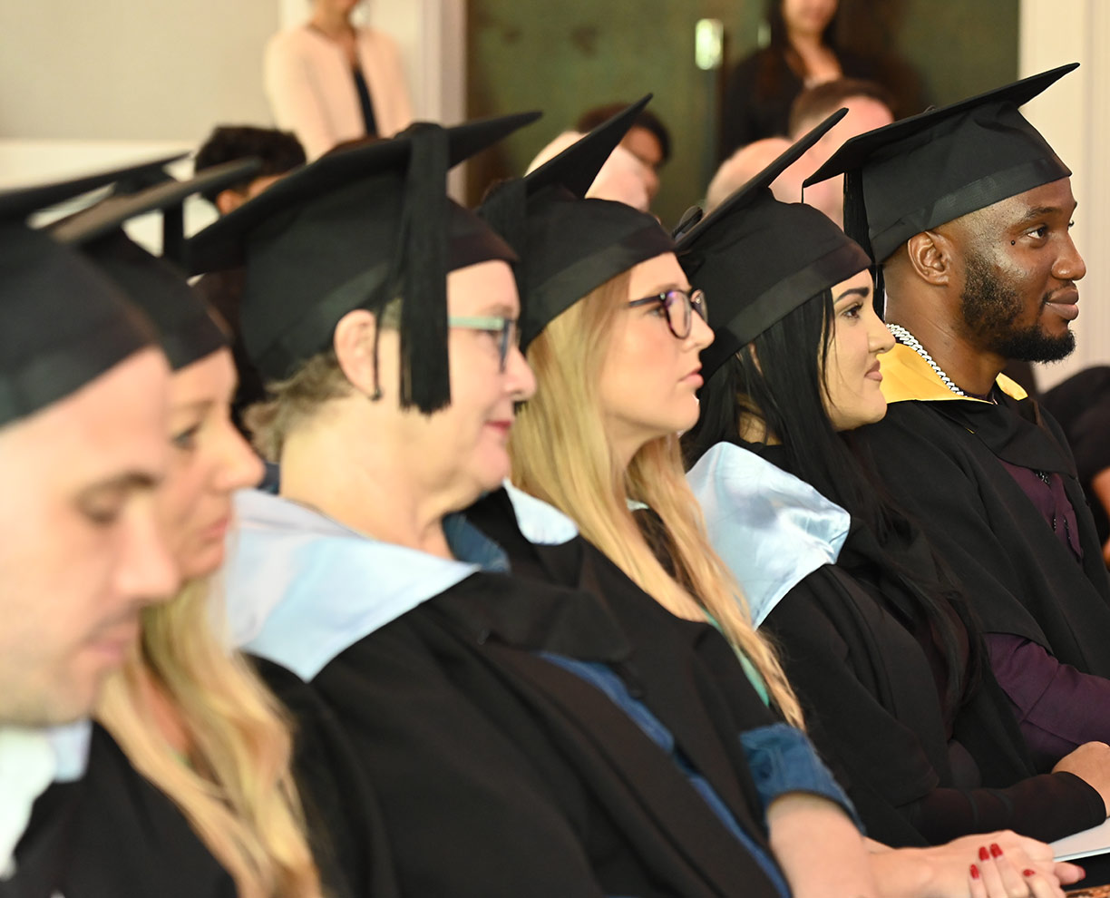 Several ACAP graduates sitting in a row at an ACAP graduation ceremony, dressed in academic regalia 1224x990