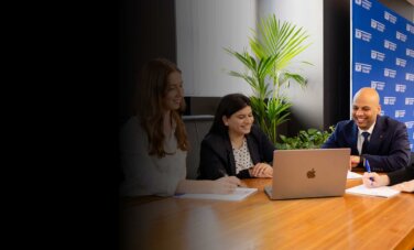 Four Law (PLT) students from ACAP University in Melbourne sitting around a desk in front of notepads and a laptop (2880x1188)