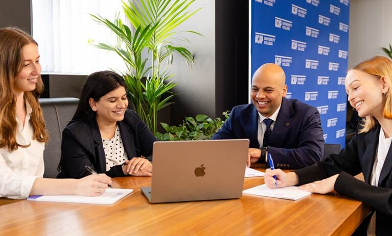 Four Law (PLT) students from ACAP University in Melbourne sitting around a desk in front of notepads and a laptop (828x676)