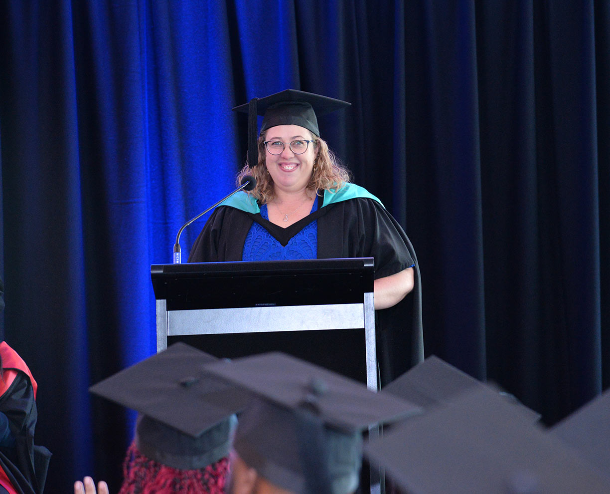 A recent ACAP graduate standing on stage in front of a lectern at an ACAP graduation ceremony (1224x990)